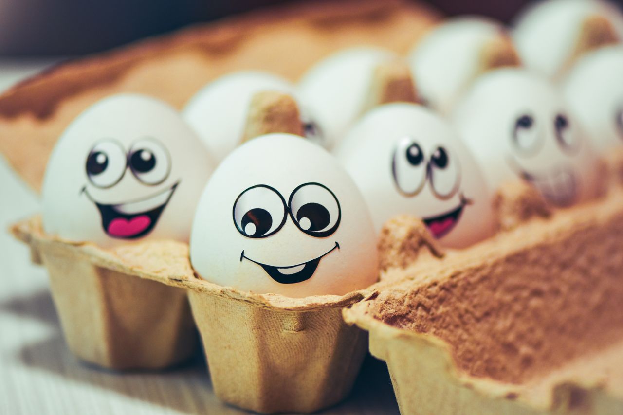 Close-up of chicken eggs with cheerful cartoon faces in an egg carton, symbolizing fun and creativity.