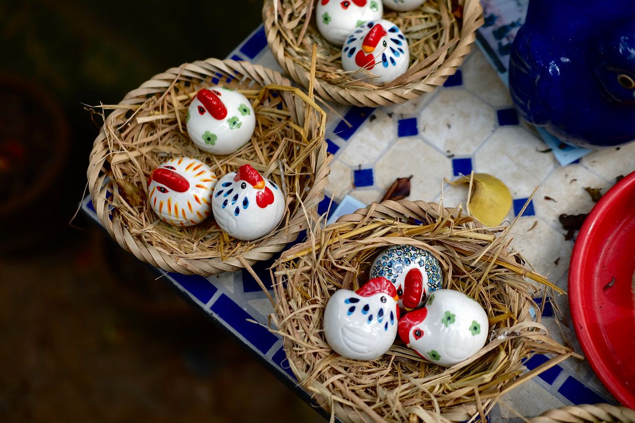Artistic ceramic chickens in straw nests on a blue-tiled table, showcasing vibrant craft designs.